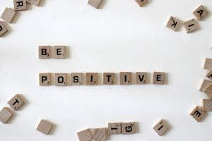 Be positive written with wooden blocks on a white surface.
